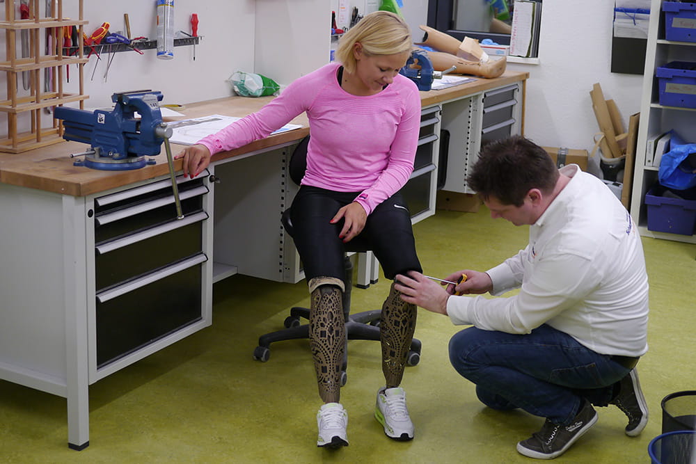 Vanessa Low sitzt in der Werkstatt und ein Techniker nimmt Feineinstellungen an der Prothese vor