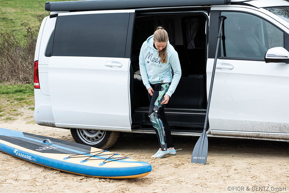 Eine Frau mit ganzbeinorthese bereitet sich am Auto auf das Stand Up Paddling vor.