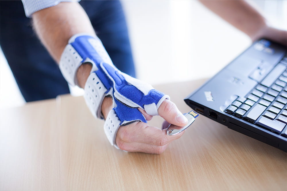 Ein Mann mit Handbandage führt gerade einen USB Stick in den Laptop.