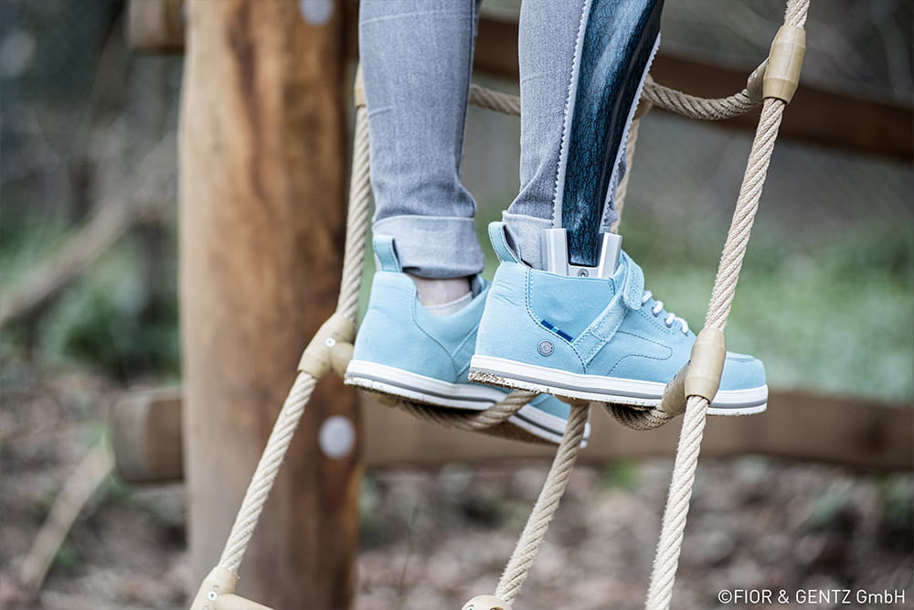 Ein Kind mit Beinorthese und Orthesenschuhen steht auf einem Klettergerüst.