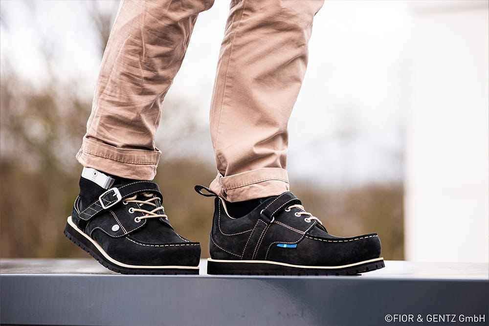 Ein Mann trägt dunkle Orthesenschuhe und eine helle Hose.