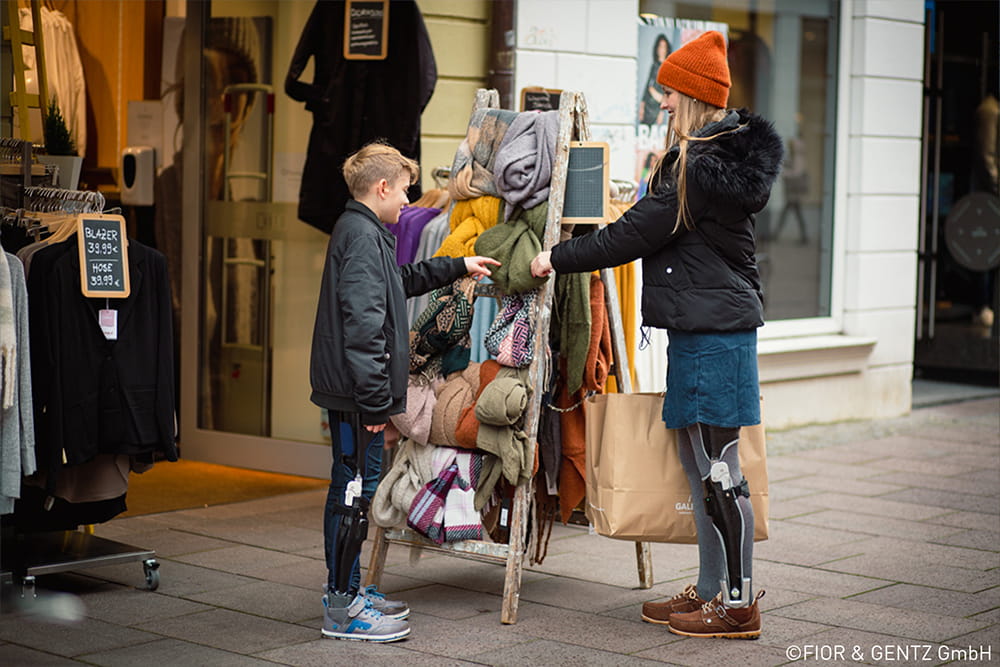Eine Muter und ihr Sohn testen gerade neue Mützen, beide tragen eine Beinorthese.