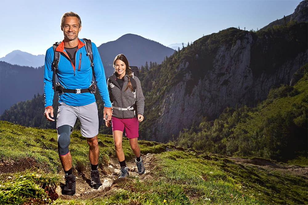Ein Pärchen wandert in den Bergen und der Mann trägt eine Beinbandage von medi.