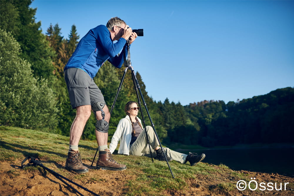 Ein Mann mit Beinorthese steht auf einer Lichtung und fotografiert.