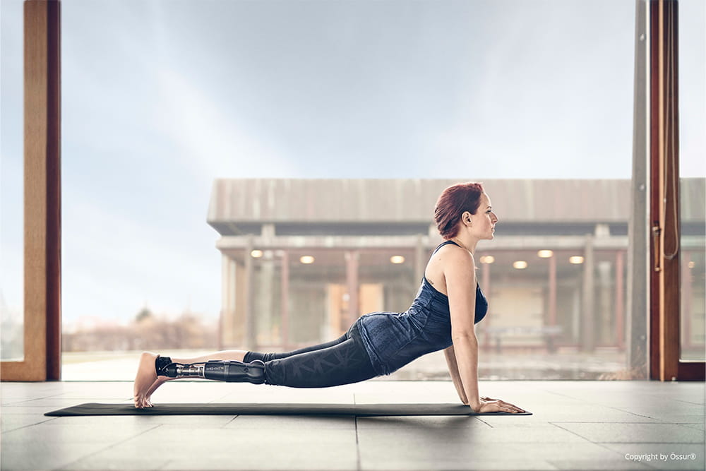 Eine Frau auf einer Sportmatte dehnt sich gerade. Man sieht, dass sie eine Beinprothese trägt.