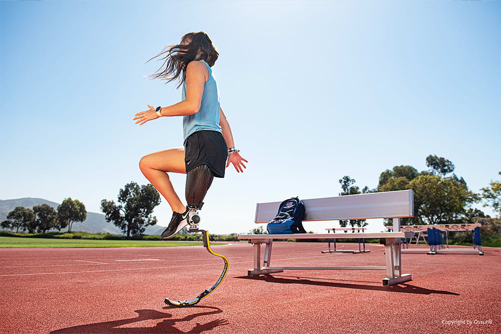 Eine Frau mit Sportprothese steht auf der Laufbahn und wärmt sich auf.