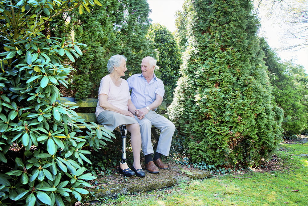 Ein älteres Paar sitzt zusammen auf einer Parkbank und die Dame trägt eine Oberschenkelprothese.