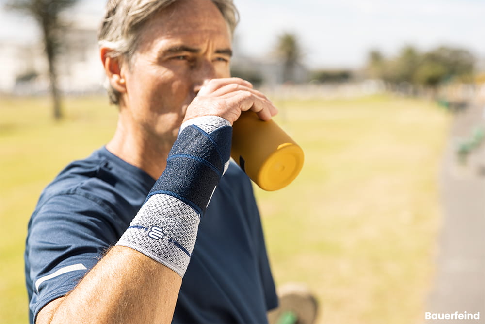 Ein Mann mit einer Handbandage trinkt nach dem Sport gerade aus einer Flasche.