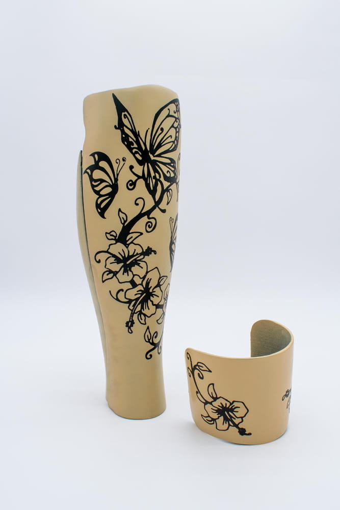 Ein Prothesencover in beige mit schwarzem Muster, das Blüten und einen Schmetterling zeigt.